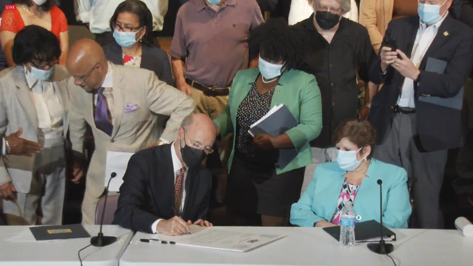 Gov. Tom Wolf signs a letter calling on state Republicans to advance a $15 minimum wage bill such as the one sponsored by state Sen. Christine Tartaglione, D-Philadelphia, who is looking on at right. (Source: Pa.gov)