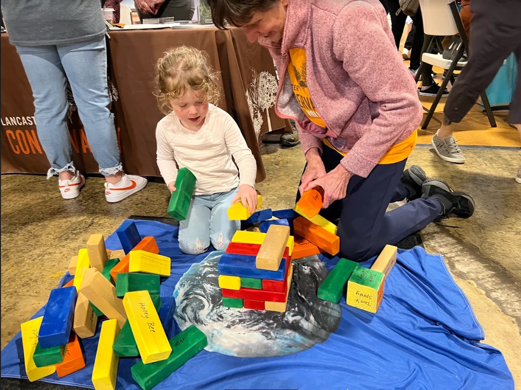 A Lancaster Conservancy volunteer gives Becky Turnbull's daughter Eden some pointers in playing "Meadow Ecology Jenga." (Photo: Kylie Stoltzfus)